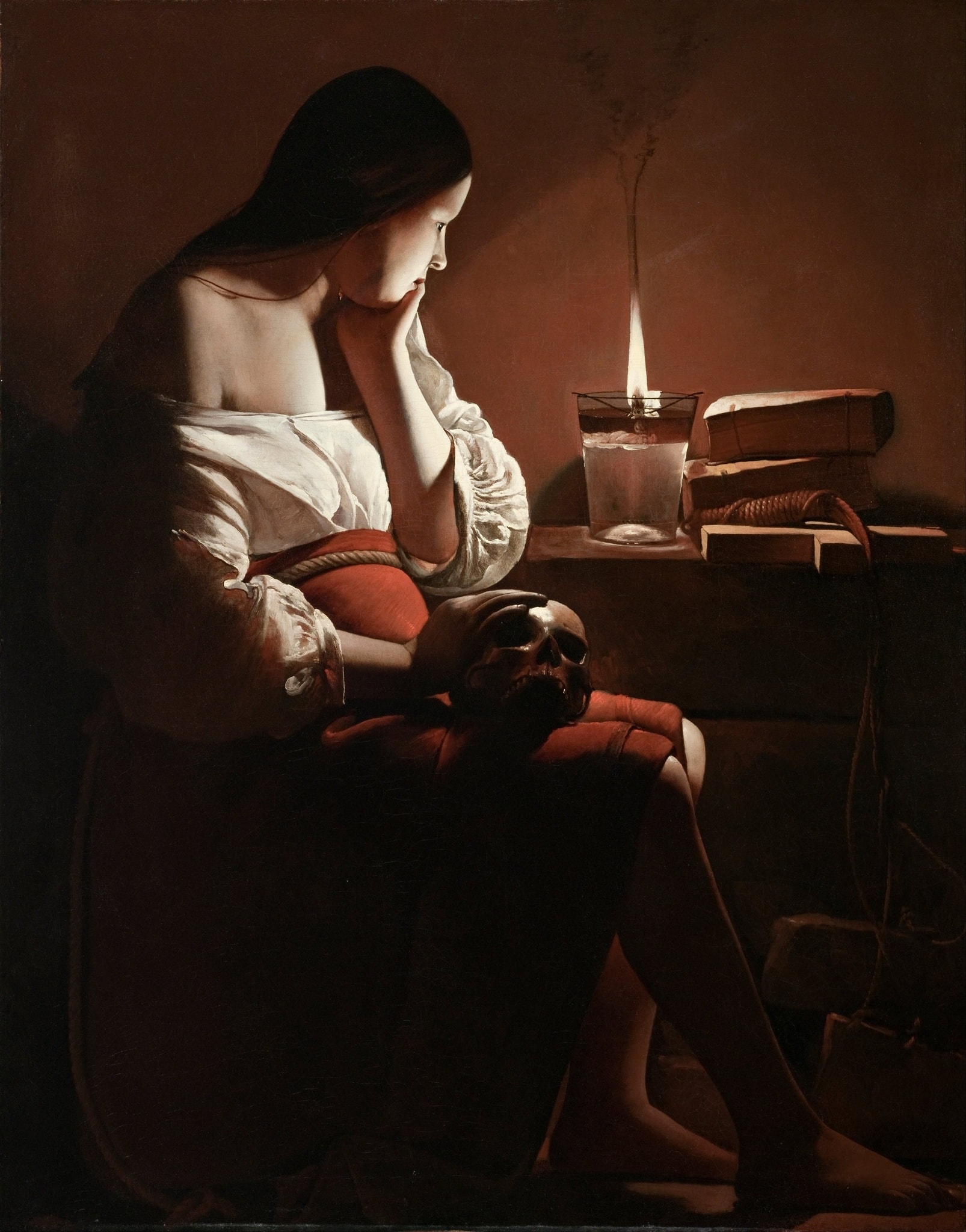 A glass oil lamp burns beside stacked books on the right. Magdalen supports her cheek with one hand and keeps the skull in her lap.