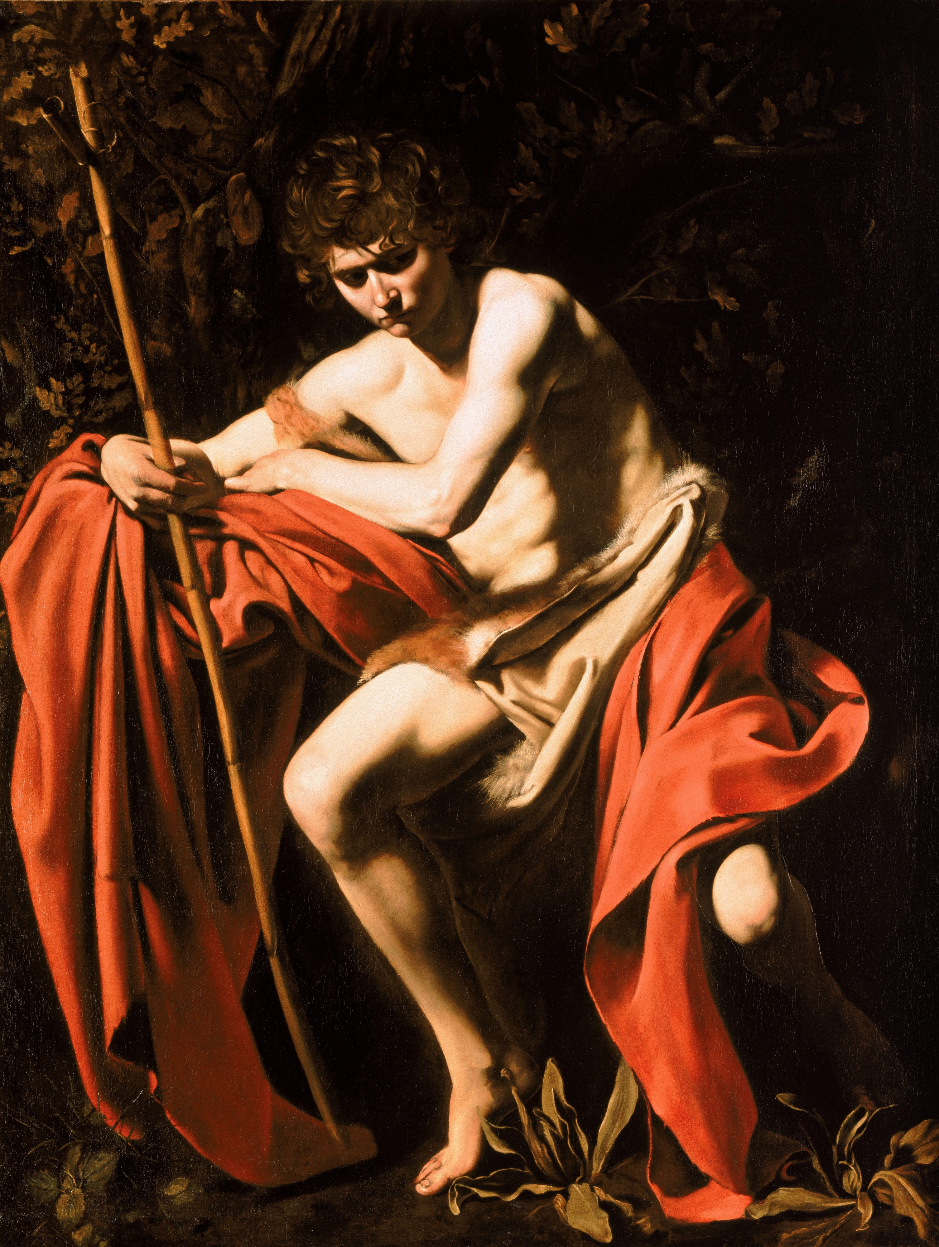 A young John the Baptist sits with his head bowed in a dark wooded landscape, a red cloak gathered around him and a reed cross beside his arm.