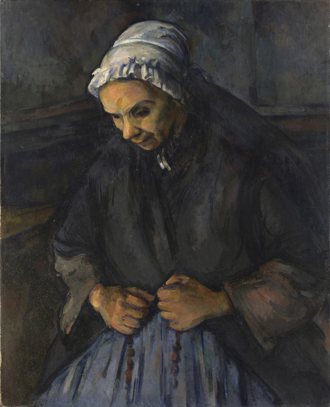 An elderly woman in a white cap sits with her head bowed and a rosary held in both hands.