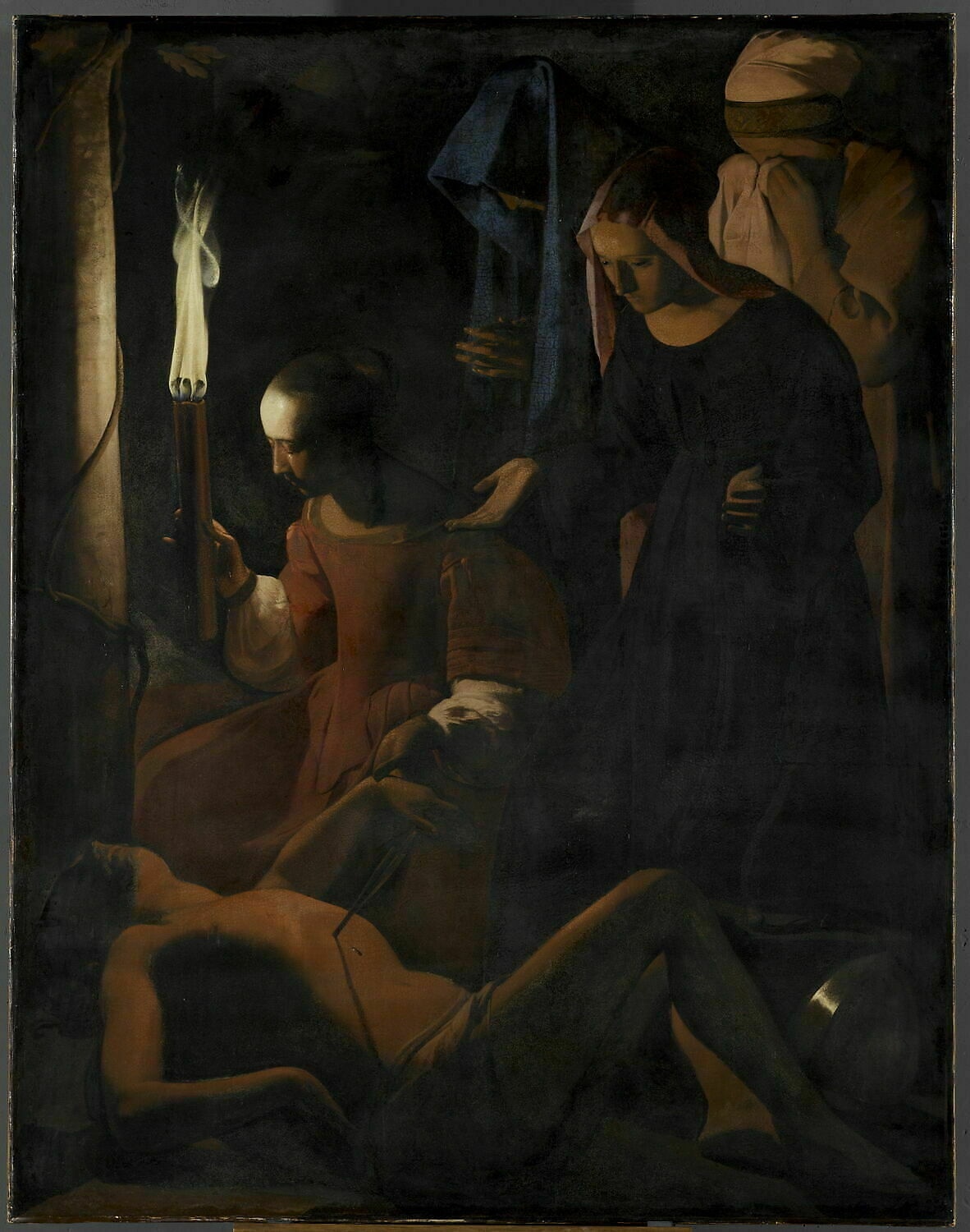 Four women gather around the reclining Sebastian in darkness; one holds a tall flame and another covers her face with a cloth.
